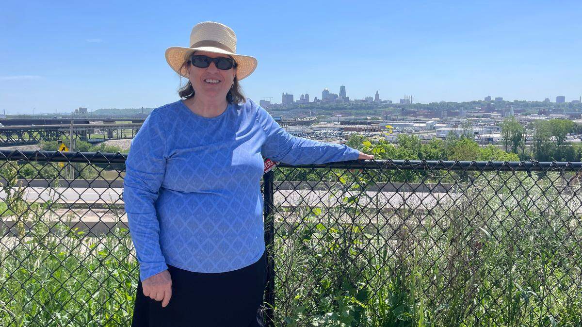 Rose Eilts, president of the Strawberry Hill Neighborhood Association, stands at the fence in front of her property with the Kansas City skyline in the background.