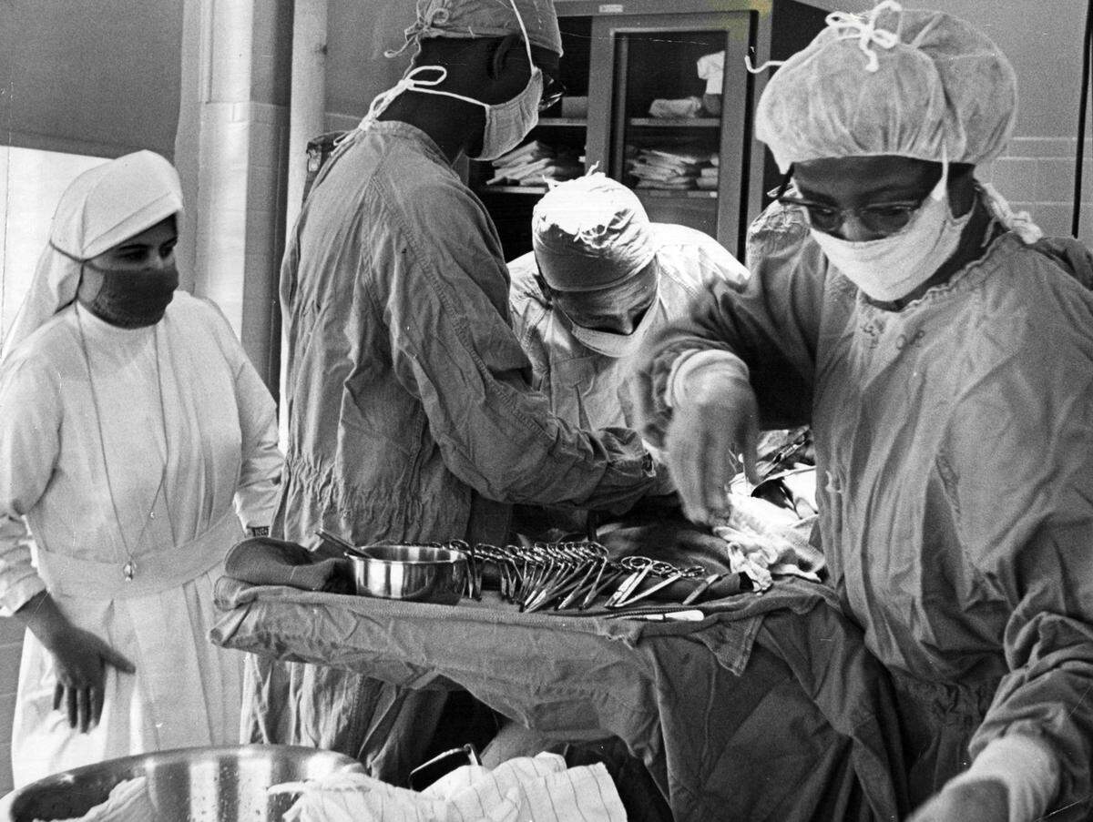 Black doctors Walter R. Peterson and Carl Peterson assist a white surgeon at Queen of the World Hospital.
