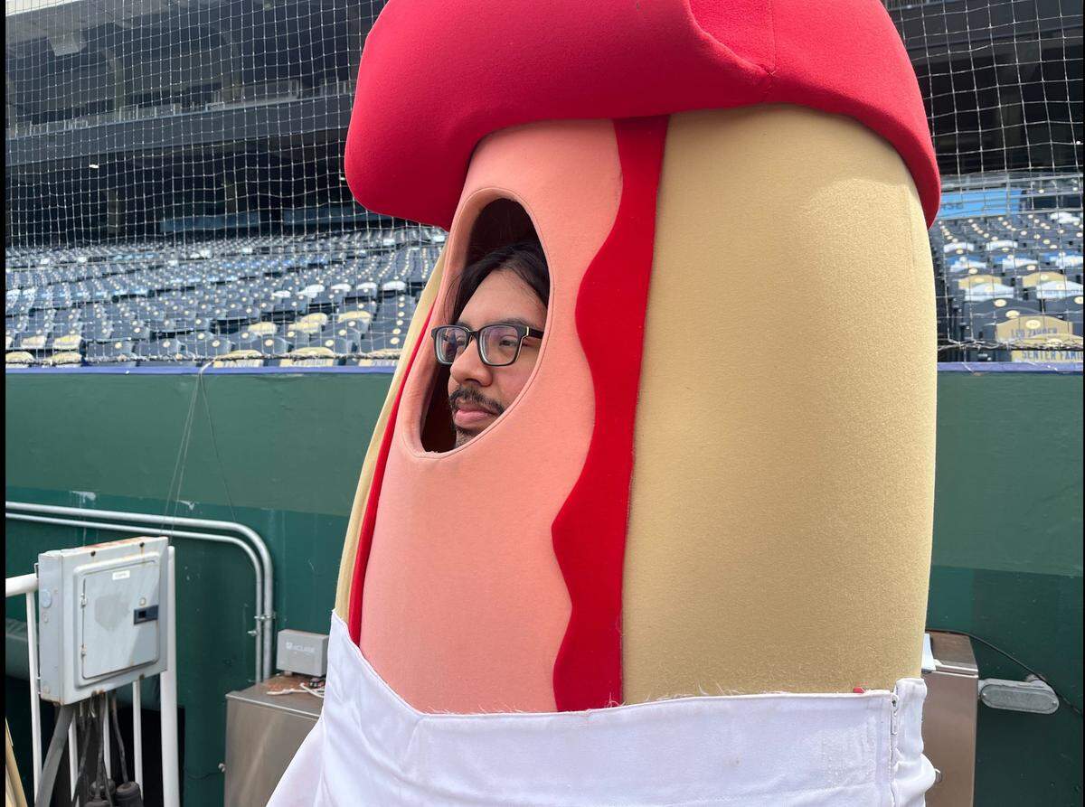 Star reporter Joseph Hernandez ponders how he got here, as he waits to run 100 yards in a hot dog costume at Kauffman Stadium. The hot dog derby is a Royals game day tradition.