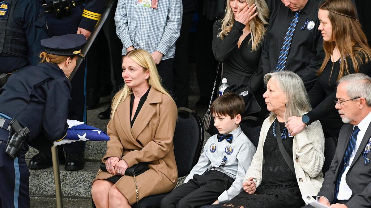 Kansas City Police Chief Stacey Graves, left, presents a flag to Cassie Muhlbauer, widow of fallen Kansas City Police Officer James Muhlbauer, 42, during the funeral for Muhlbauer and his police K-9, Champ, Wednesday, Feb. 22, 2023, at Municipal Auditorium in Kansas City. Muhlbauer’s family, right, looks on.