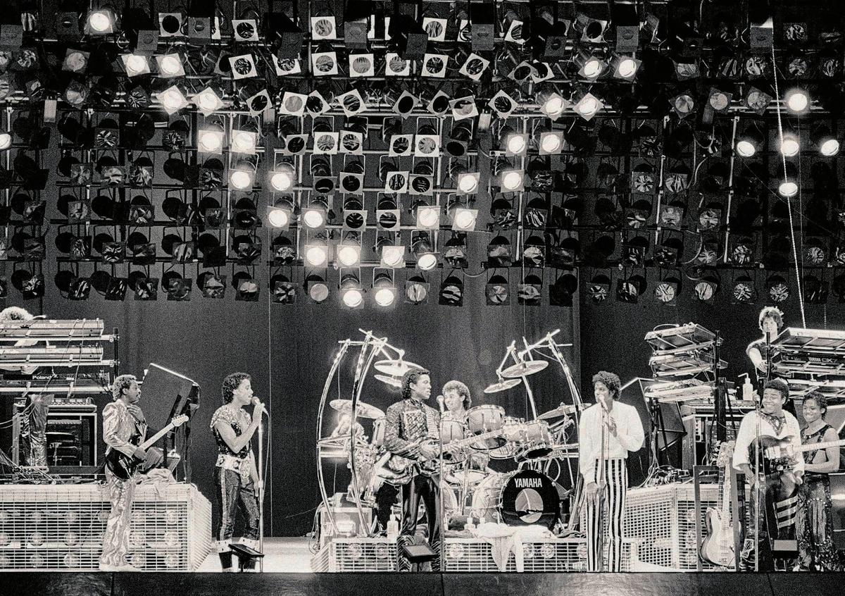 The lights above the stage make a “V” as the Jacksons kick off their “Victory Tour” at Arrowhead Stadium onJuly 6, 1984. The concert includes laser lights, fireworks and a five-story stage. Shown are Marlon Jackson, second from left, Jermaine, third from left, Michael, in striped pants, Tito, second from right, and Randy, right. The other members of the band are not identified. The Jacksons were to perform across the U.S. and Canada for five months.