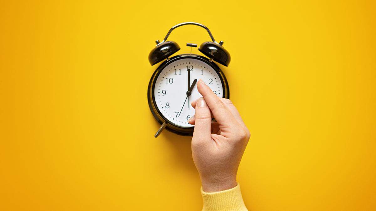 Daylight saving day. Fall Back. Black Alarm clock and female hands on yellow background. Daylight saving time end