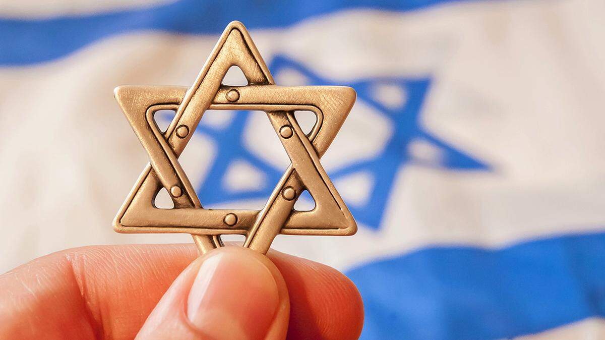 Hand holding a Star of David (”Magen David”) with Israeli flag on the background. Hidden Jewish identity concept. jew antisemite antisemitism anti-semite anti-semitism