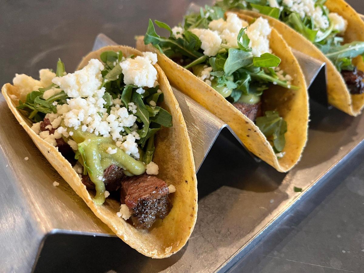 Three carne asada tacos are served on a metal taco holder tray at Mission Taco Joint in Kansas City.