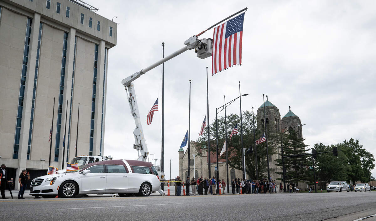The hearse carrying the casket of Wyandotte County Sheriff’s deputy Elijah Ming passes under a flag in front of the Wyandotte County Unified Government offices during the funeral procession as it passed through downtown Kansas City, Kansas, on Monday, August 11, 2025.
