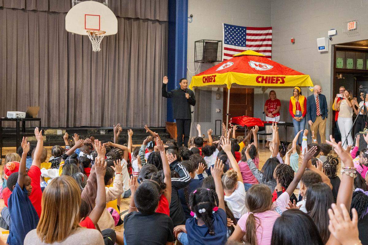 Kansas City Chiefs cornerback Trent McDuffie raises his hand with the students at Gordon Parks Elementary School during a meet & greet and backpack drive on Monday, Aug. 25, 2025, in Kansas City. In addition to signing autographs, McDuffie donated the backpacks, which also included water bottles and school supplies, to 150 kids at the school through his T22 McDuffie Foundation.