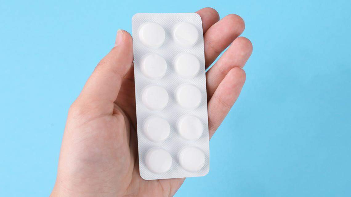 Woman holding pills near paper note with word Abortion on light blue background, top view medication chemical medical 