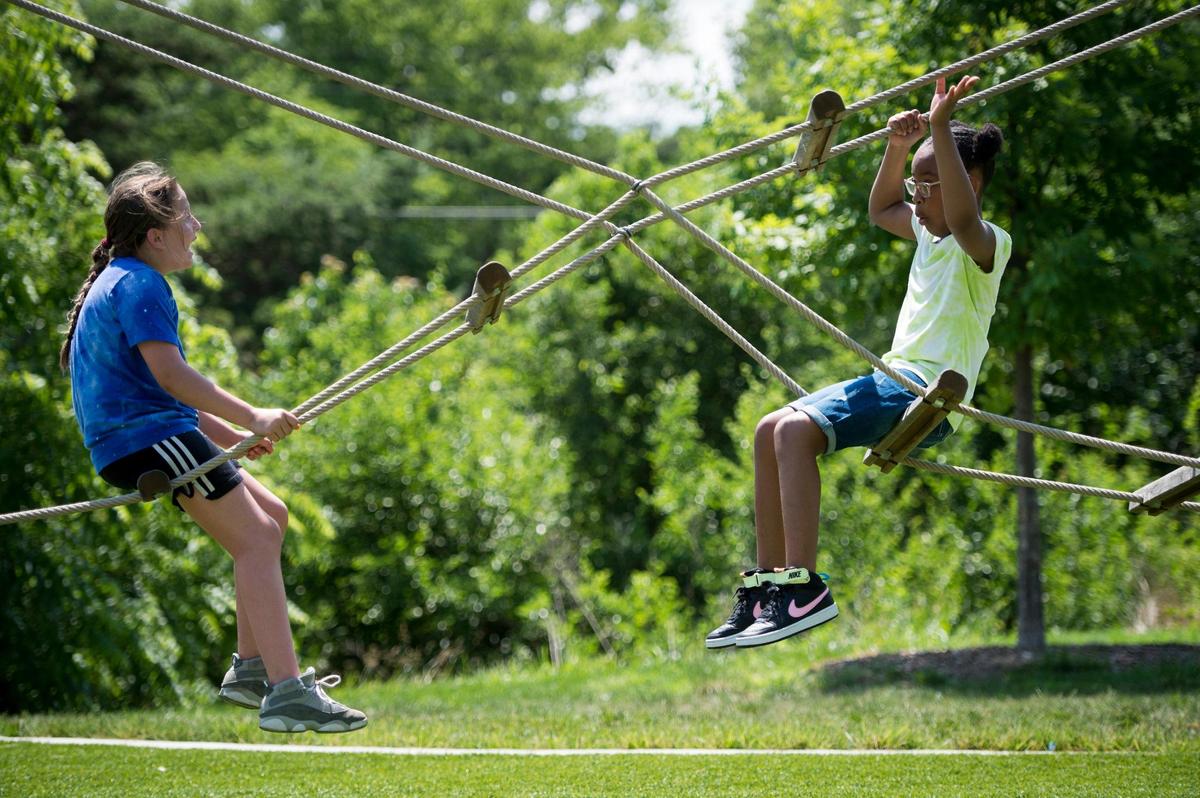 Lily Orozco, 9, left, of Overland Park and Londyn Walker, 8, of Raytown, chatted as they balanced on the ropes on the tree line adventure during a visit Tuesday to Meadowbrook Park in Prairie Village.