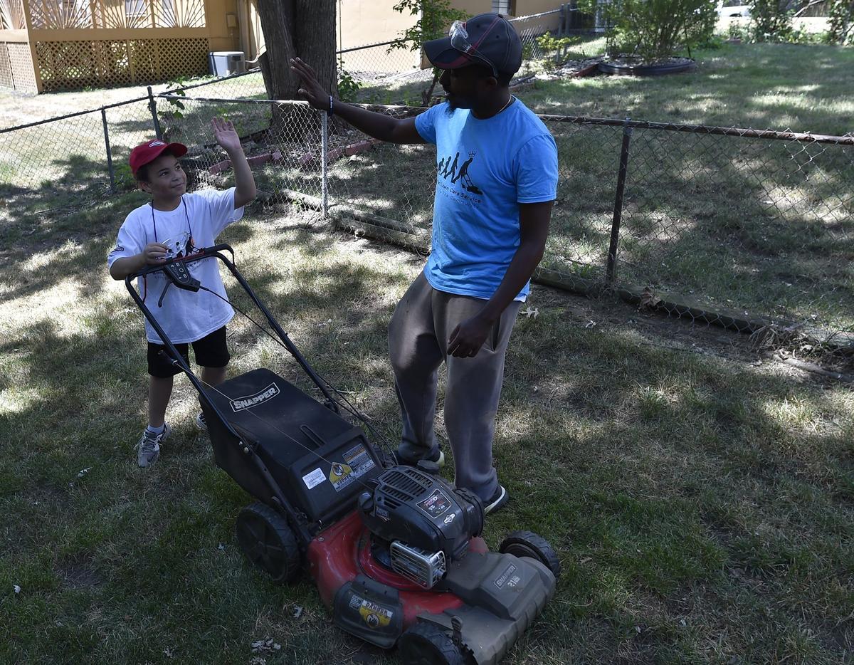 Rodney Smith, right, of Huntsville, Alabama, gives a high five to Erron Blockmon, 9, of Lee's Summit, after they finished mowing a lawn Tuesday afternoon in Overland Park.  Smith aims to help mow lawns for elderly, veterans or single moms in all 50 states. He calls his effort, "Making a difference one lawn at a time." Smith has only four more states to go after his stop in Kansas.