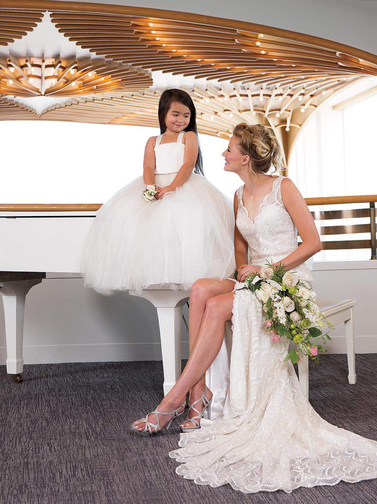 SITTING PRETTY On bride: Madison James scalloped lace gown with floating buttons, $1,538, from Stephanie's Bridal Boutique. Pelle Moda strappy silver heels, $89.90, from Bob Jones Shoes. On flower girl: Amalee dress with satin top and tulle skirt, $238, from Stephanie's Bridal Boutique. Bridal bouquet and corsage from Craig Sole Designs.