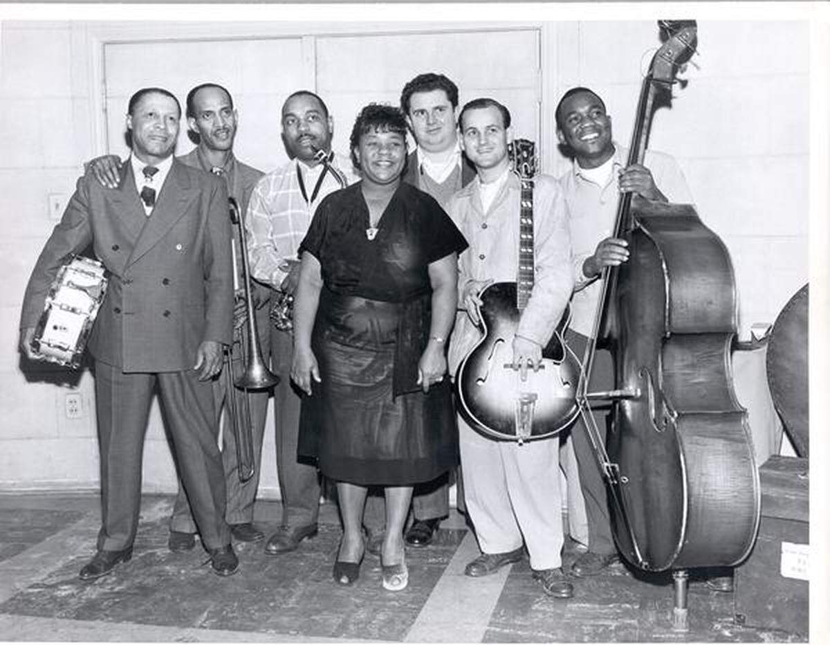 Julia Lee and Her Boy Friends at a Capitol Records recording session: Samuel “Baby” Lovett holding a snare drum, Vic Dickenson with a trombone, Benny Carter with a saxophone, Lee (center), Dave Cavanaugh with a saxophone, Jack Marshall with a guitar and Billy Hadnott with a double bass.