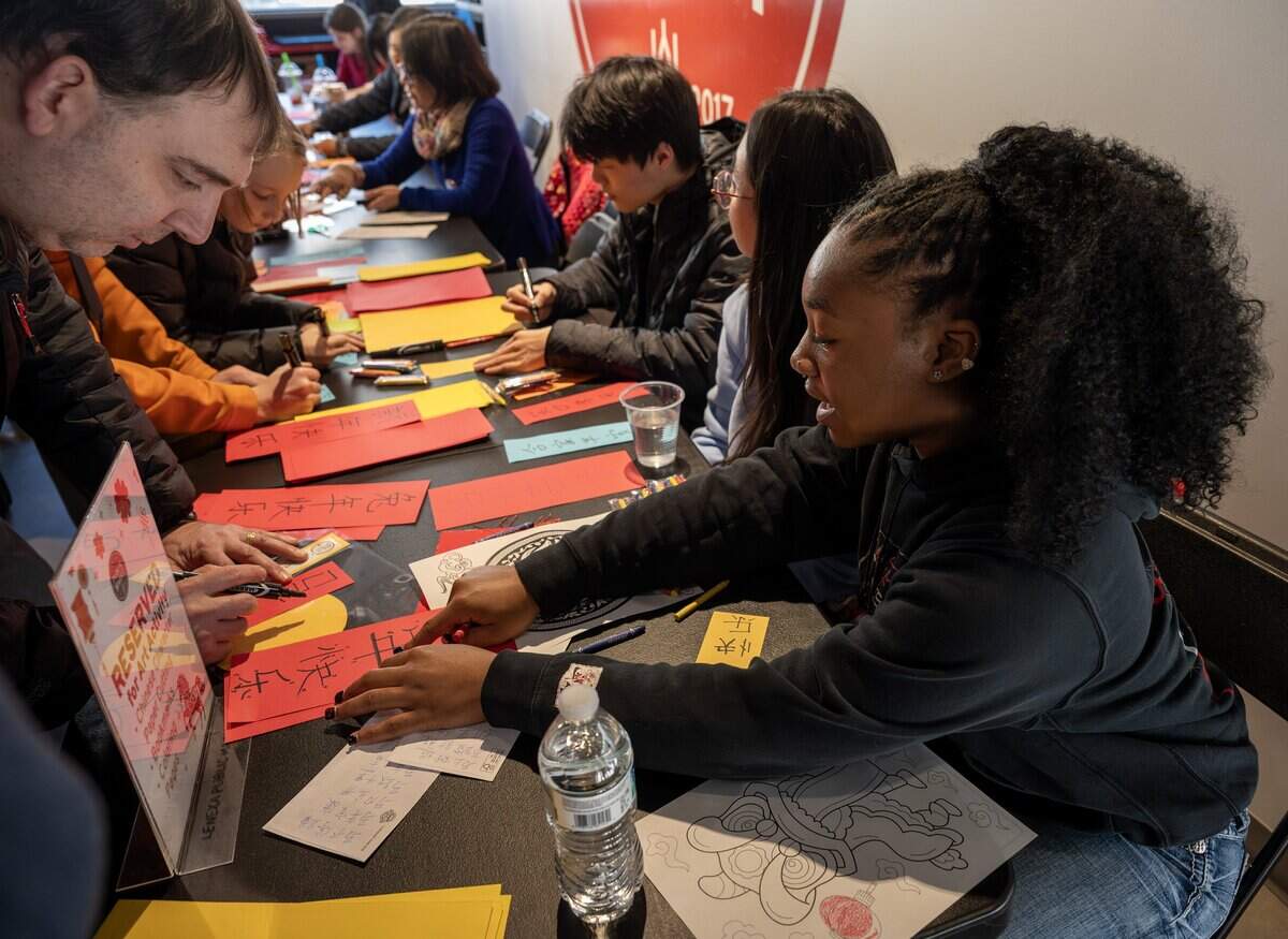 Seventeen-year-old Giah Burns, a student volunteer with the Lee's Summit West High School National Chinese Honor Society, helps a guest practice Chinese characters during a Lunar New Year celebration at the Lenexa Public Market on Sunday, Feb. 22, 2026, in Lenexa.