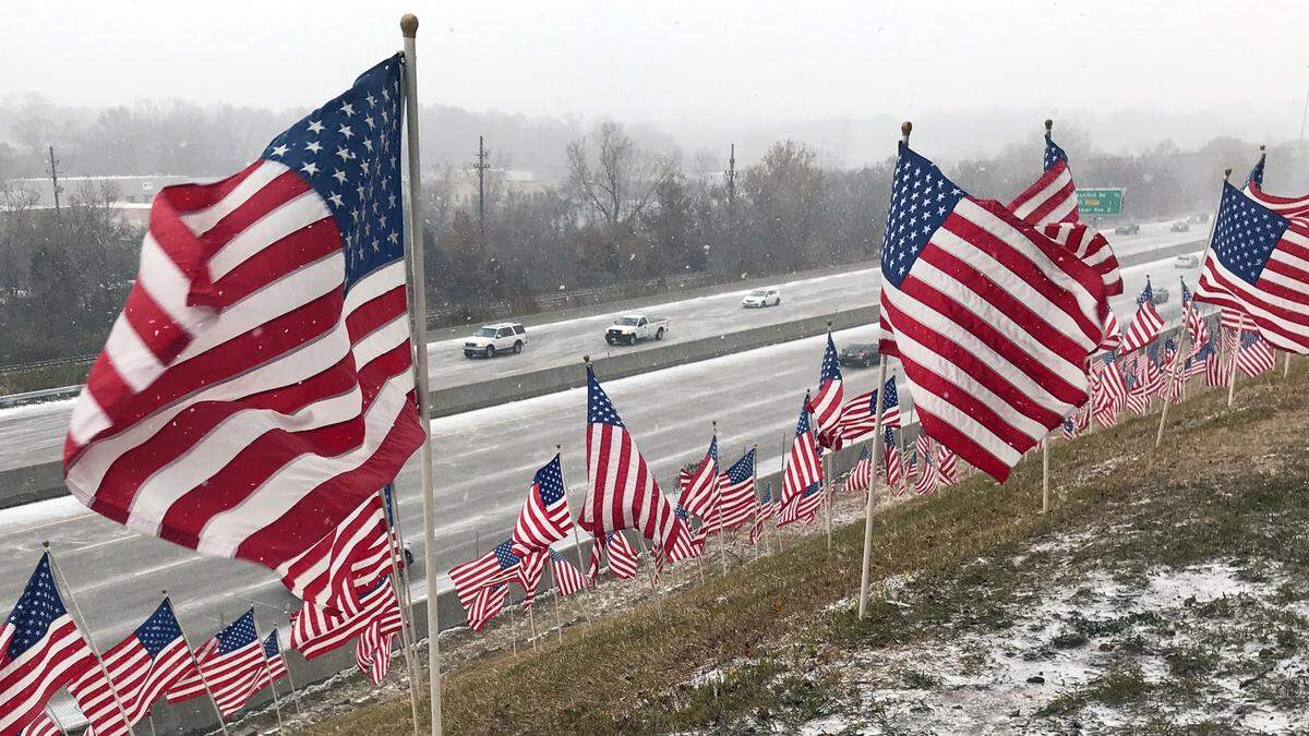Snow blows over Interstate 35 in Merriam near a Veterans Day flag display Monday. Drivers were being urged to use caution because road conditions could deteriorate and become icy.