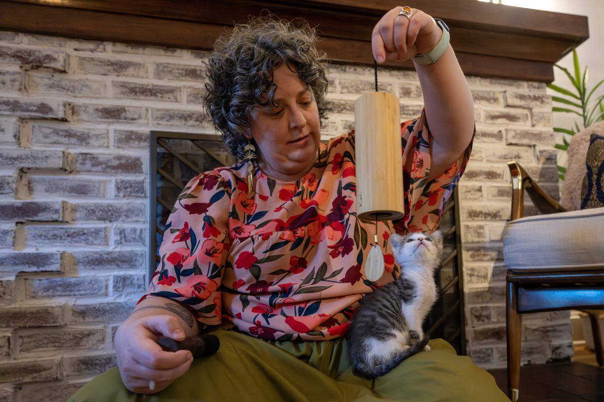 Joann Schermerhorn plays a chime as a foster kitten named Buckwheat sits on her lap during a sound bath session Thursday, Aug. 7, 2025, in Kansas City, Mo. Schermerhorn uses singing bowls, chimes and other instruments to help calm stressed cats.