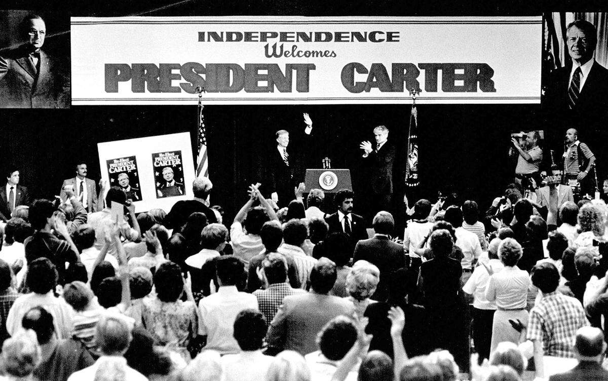 Mrs. Bess Truman waiting for Carter to arrive for a brief visit this morning. President Carter takes a look at the reproduction of President Truman’s Oval Office at the Truman Library in Independence. ***** is 6-year-old son, Clay, try to fan away the heat as they meeting.