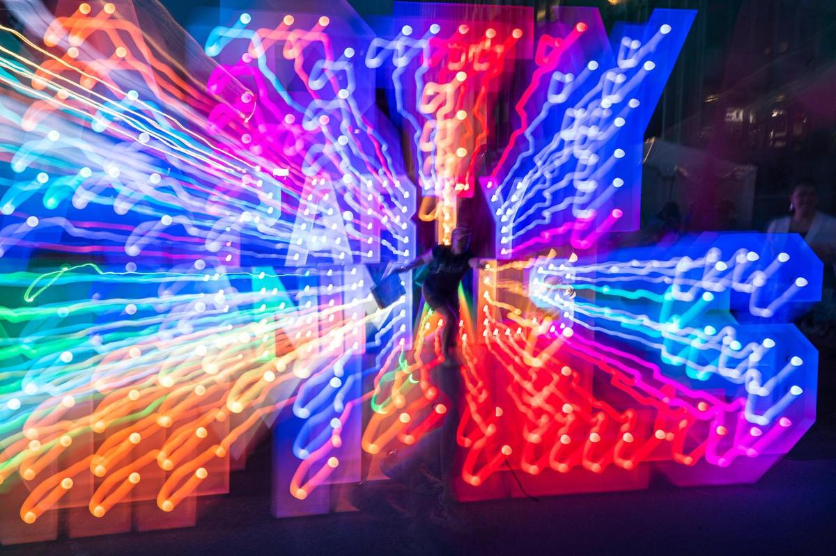 A Boulevardia attendee stands for a photo in front of a neon light sign at Boulevardia on Friday, June 16, 2023, in Kansas City. 