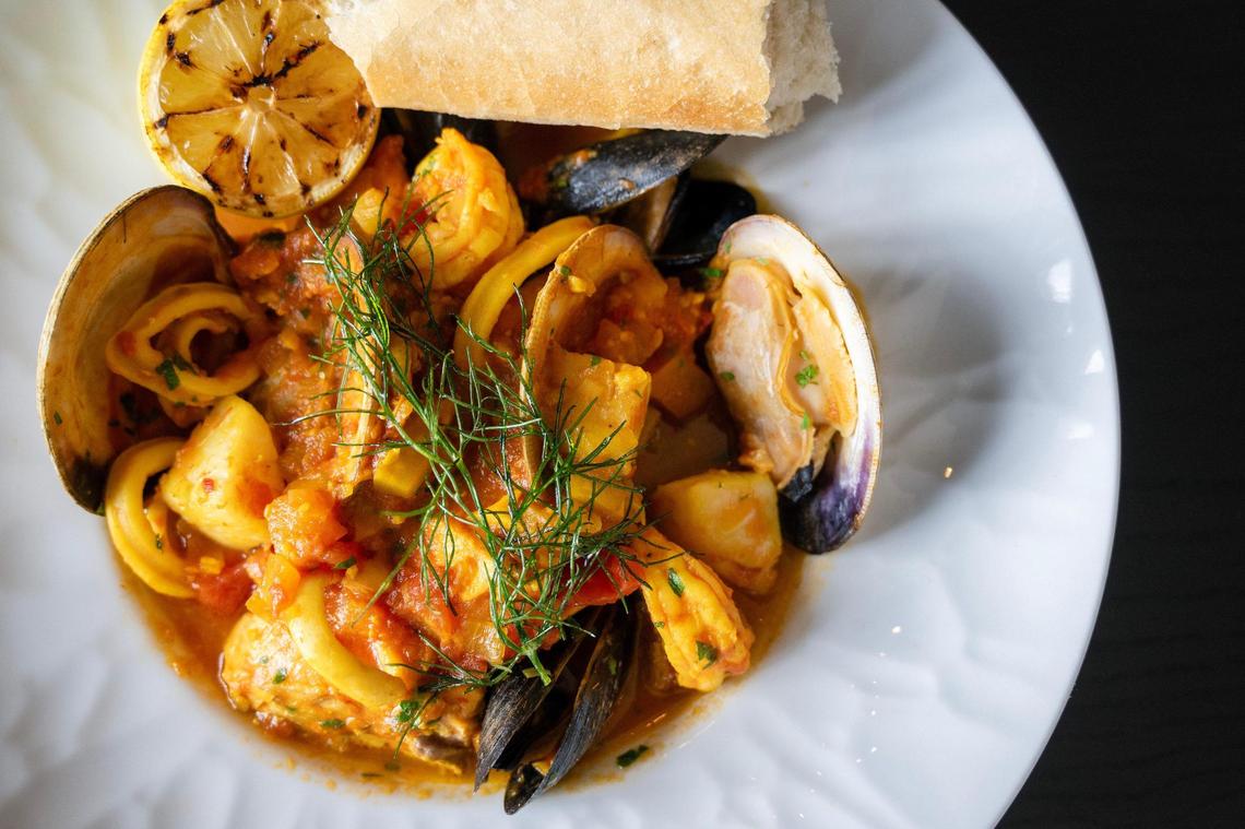 The seafood and saffron dish has clams, oysters, calamari and mussels, served in a vegetable and tomato saffron broth alongside a slice of lemon and a French baguette.