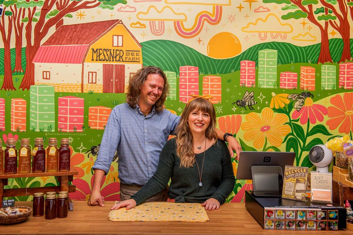 The Messner Bee Farm Store has a colorful interior, designed by Rachael in collaboration with Erik and their team. The Messners smile in front of a large mural featuring bees at the Messner Bee Farm is displayed on one wall.