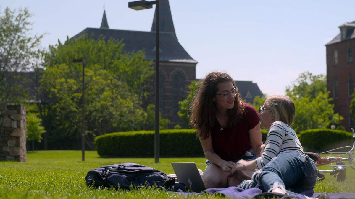 Renate Rose of Olathe, left, shown with girlfriend Tayla at Gallaudet University, talks about the “deaf people problems” that hearing people might never have considered. The makers of the series created a detailed description of this photo to help make it accessible to more people. It has been slightly edited to follow The Star’s guidelines: Renate Rose is a white female who has dark curly hair and is wearing glasses and a red T-shirt. She sits on a lawn at Gallaudet with greenery around her. She is holding hands with her girlfriend. On the ground there is a backpack, a computer and a purple blanket. Her girlfriend has blond hair, glasses and is wearing jeans and a long-sleeved white T-shirt with stripes.