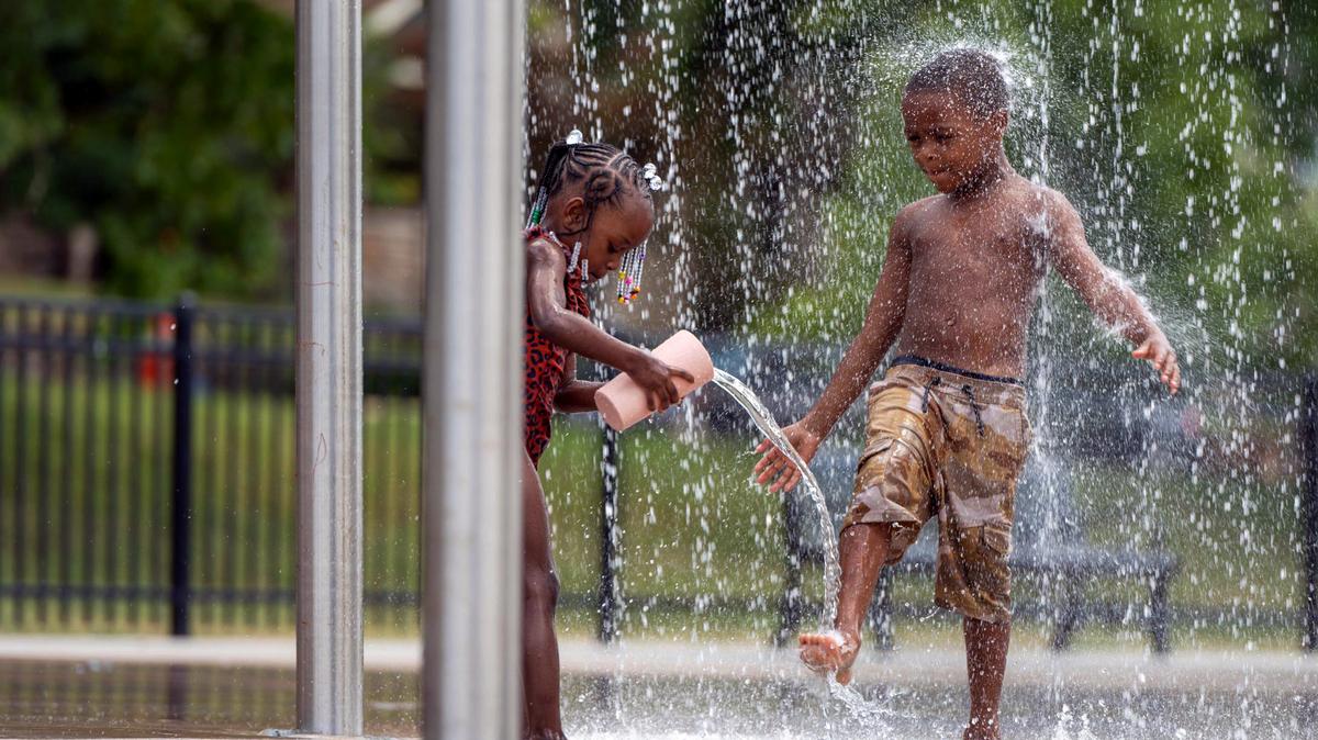 Four-year-old Malia Brooks, left, and five-year-old Prince Boyles play under a water fountain at the Sprayground in Gillham Park on Monday, July 18, 2022.