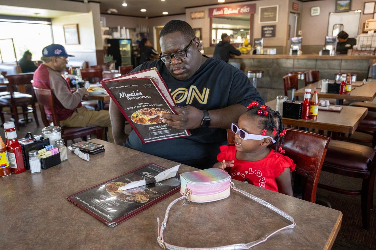 D’Mari Harding of Baton Rouge, Louisiana, looks over the menu for himself and his daughter, Grace Harding, 2, during a visit for breakfast at Niecie’s Restaurant.