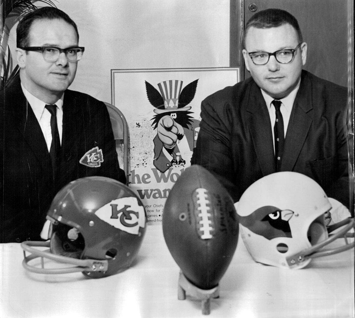 Lamar Hunt (left), owner of the Kansas City Chiefs, and Bill Bidwill, vice president of the St. Louis Cardinals of the National Football League, sit behind their teams’ helmets at a press conference in 1968. It was announced that the Chiefs and the Cardinals would face off in an exhibition game in Kansas City.