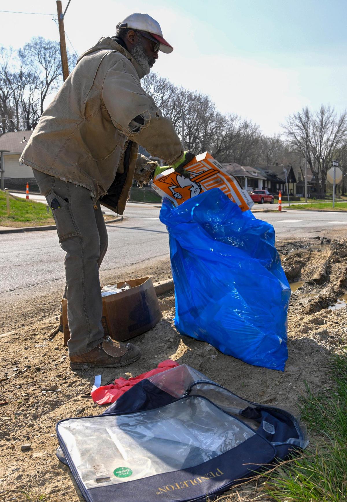 Robert Quarles of Kansas City shoves a discarded pizza box into a city-issued trash bag Tuesday, April 4, 2023, near E. 23rd Street and Askew Avenue, just off Interstate 70, in Kansas City. For the past 10 years, Quarles has been voluntarily picking up trash and debris in Kansas City. He gets rolls of 150 blue trash bags from the city.