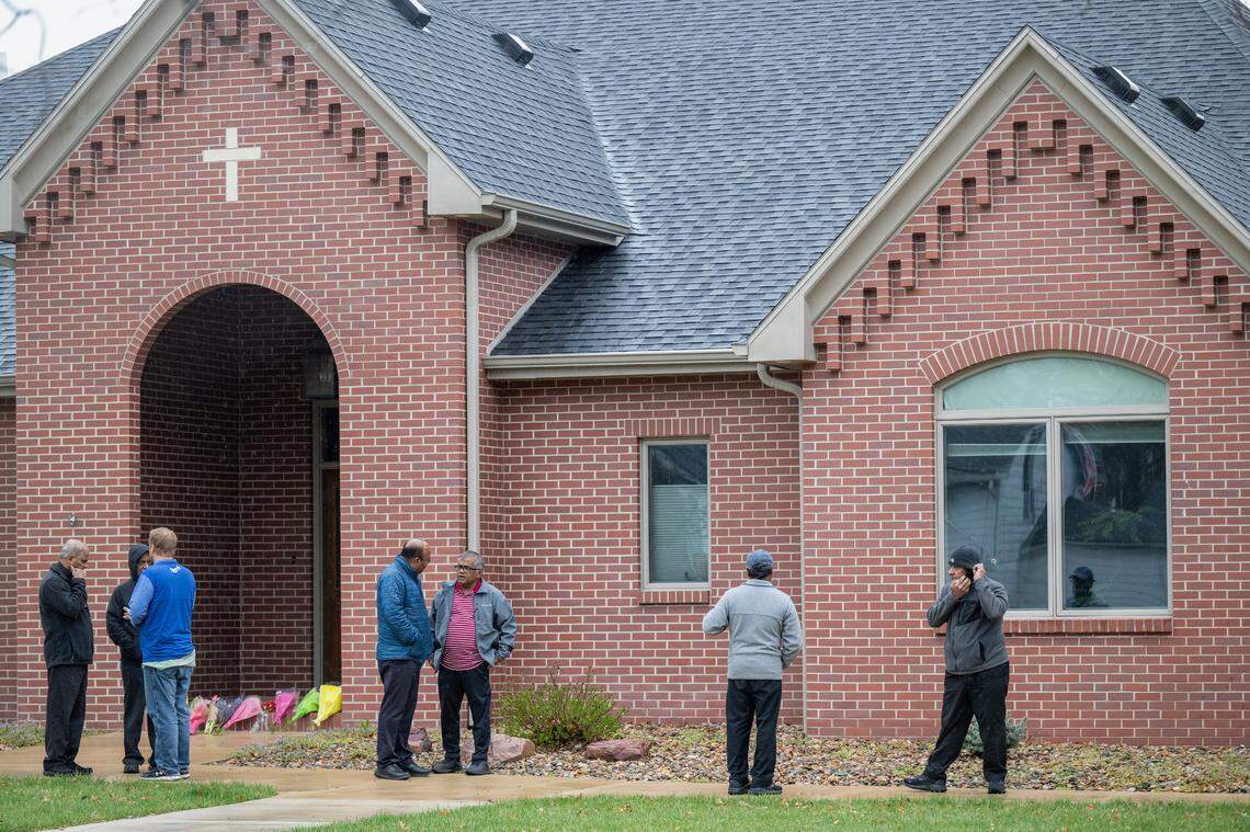 Men gathered outside the rectory at the Saints Peter and Paul Catholic Church in Seneca, Kansas, on Friday, April 4, 2025, near where Fr. Arul Carasala was shot and killed on Thursday. Fr. Carasala had been the pastor of the Seneca church since 2011. A bullet hole is visible in the window. 