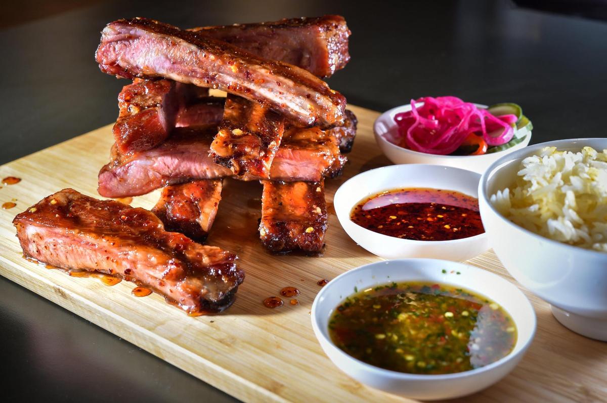A Duroc St. Louis style pork ribs feature heavenly BBQ seasoning, Sweet Chili Glaze, served with seasoned jasmine rice, house pickles, Tiger Cry Sauce and Buck Tui BBQ Sauce.
