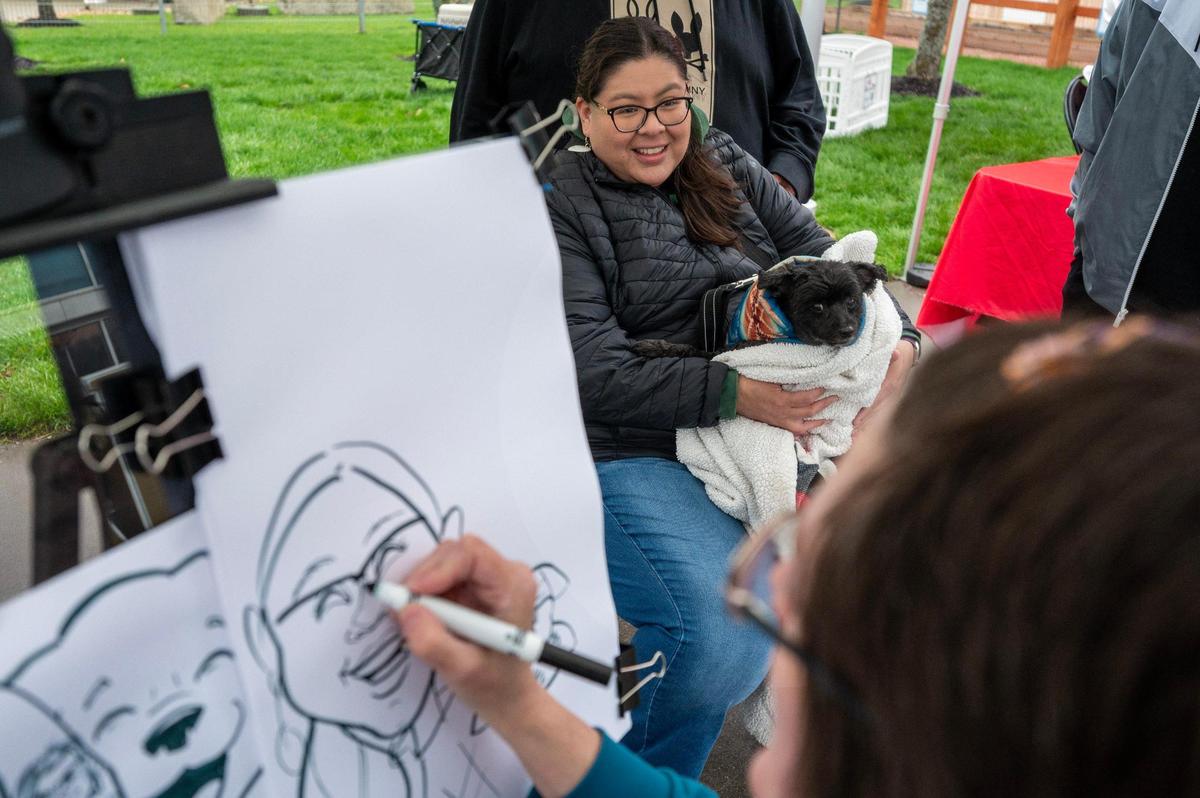 Mary Harjo and her dog, Peabody, get a caricature drawing done by artist Valerie Wolf during Bark at the Park at an MLB game between the Kansas City Royals and the Baltimore Orioles on Friday, April 4, 2025, at Kauffman Stadium.