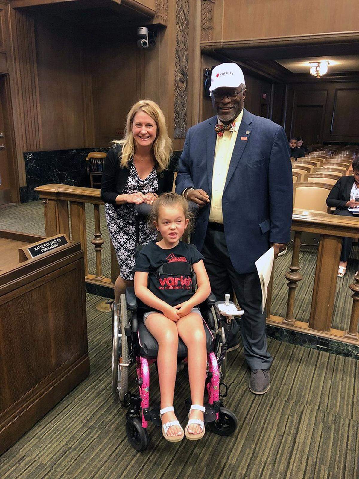 In this 2018 photo provided by the family, Heather Hall, a Kansas City Council member and then Mayor Sly James pose for a photo with Olivia Bloomfield who was a champion for children with developmental disabilities seeking for accessibility and inclusion in the city's parks, playgrounds and bathrooms.