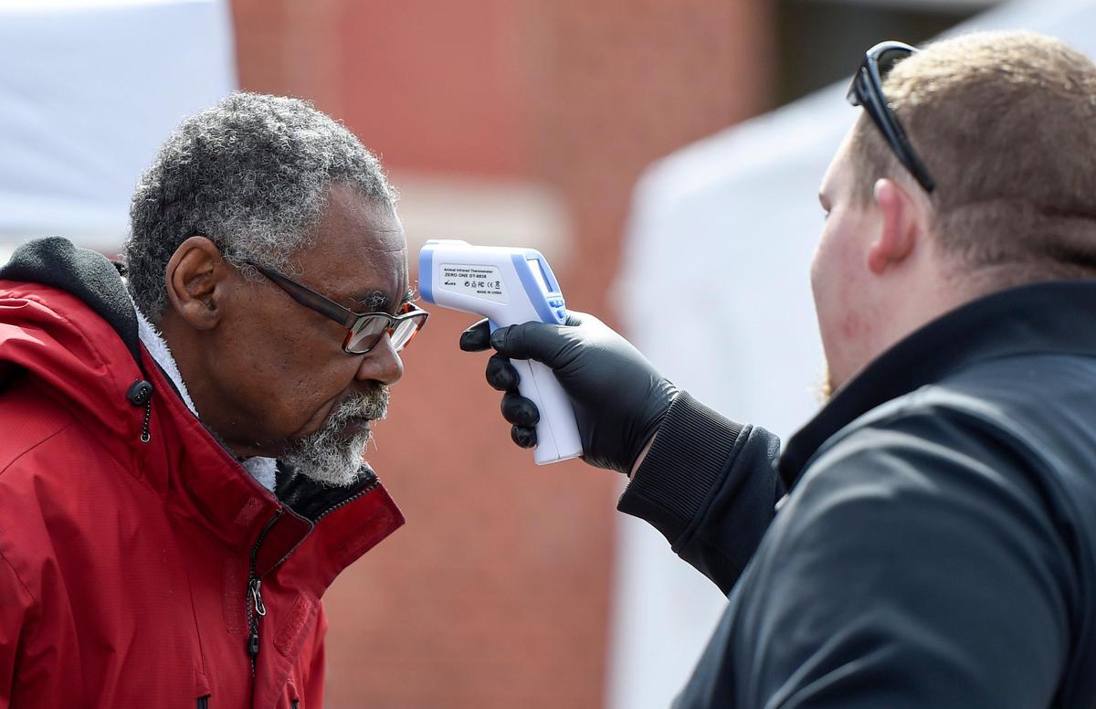 A security officer checks the temperature of a client Wednesday, outside the tent village set up by Kansas City nonprofits outside of Hope Faith Homeless Assistance Campus, 705 Virginia Ave.