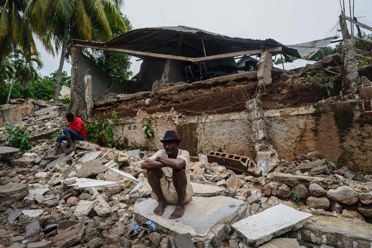 FILE - In this Aug. 17, 2021 file photo, a man crouches on the rubble of the hospital destroyed by the earthquake in Fleurant, Haiti, three days after the 7.2-magnitude quake hit the Caribbean nation. Twin tragedies on opposite sides of the world are piling misery on people that have seen far more than their share. In Haiti, yet another earthquake and yet another storm struck a country exceptionally ill-equipped to handle either.
