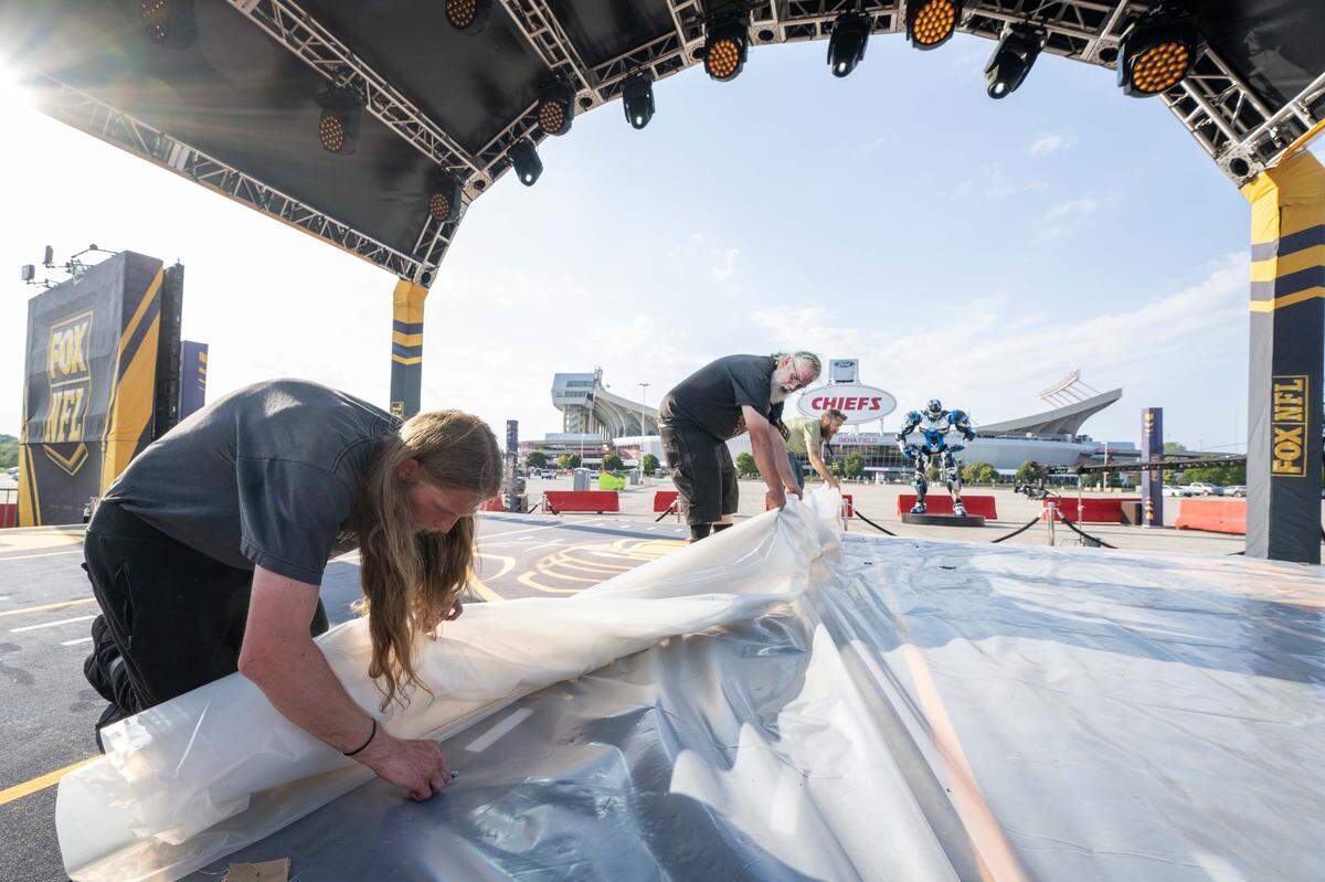 Crewmen unroll a tarp on a stage in the parking lot of GEHA Field at Arrowhead Stadium, in Kansas City, on Thursday, Sept. 11, 2025. FOX Sports is bringing their entire FOX NFL Sunday coverage team to Kansas City for the Chiefs’ home opener, a Super Bowl rematch vs. the Philadelphia Eagles.