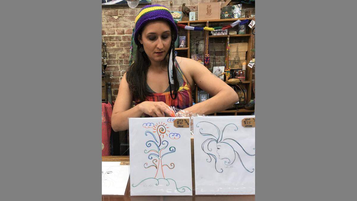 Shea LeJeune arranges her paintings in the Blue Heron Design store during a Fourth Fridays Art Walk.