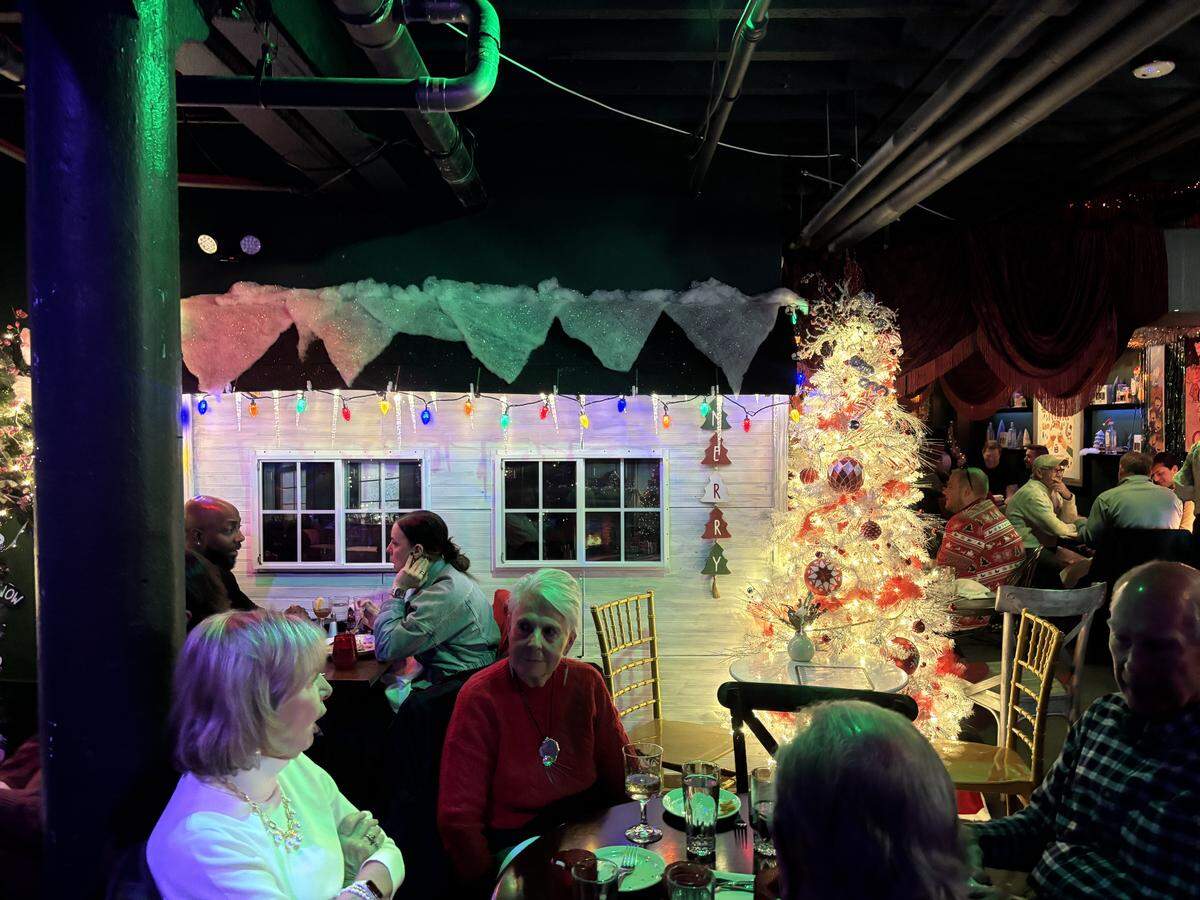 Tom’s Town customers sit in the glow of a Christmas tree inside of the Crossroads distillery’s holiday pop-up, Tinsel Town. The experience will be open until Jan. 3.