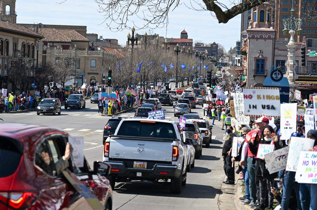 Protesters, some holding signs out of cars, gathered along the Country Club Plaza on Saturday, March 28, 2026, in Kansas City for a No Kings protest against the Trump administration.
