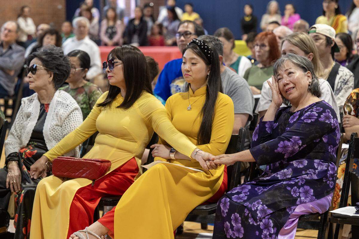 Members of the Vietnamese community including Hoa Tran, from left, her daughter, Hue Pham, and Nancy Dinh-Pham, her, her granddaughter, held hands with Tina Lê, right, who wiped a tear from her eye as her daughter, Béty Lê Shackelford, paid tribute to Lê during  "Remembering Saigon,” a remembrance event marking of the 50th anniversary of the end of the Vietnam War on Sunday, May 4, 2025, at the Don Bosco Community Center in Kansas City.  Many of the people in attendance fled South Vietnam, including Lê. 