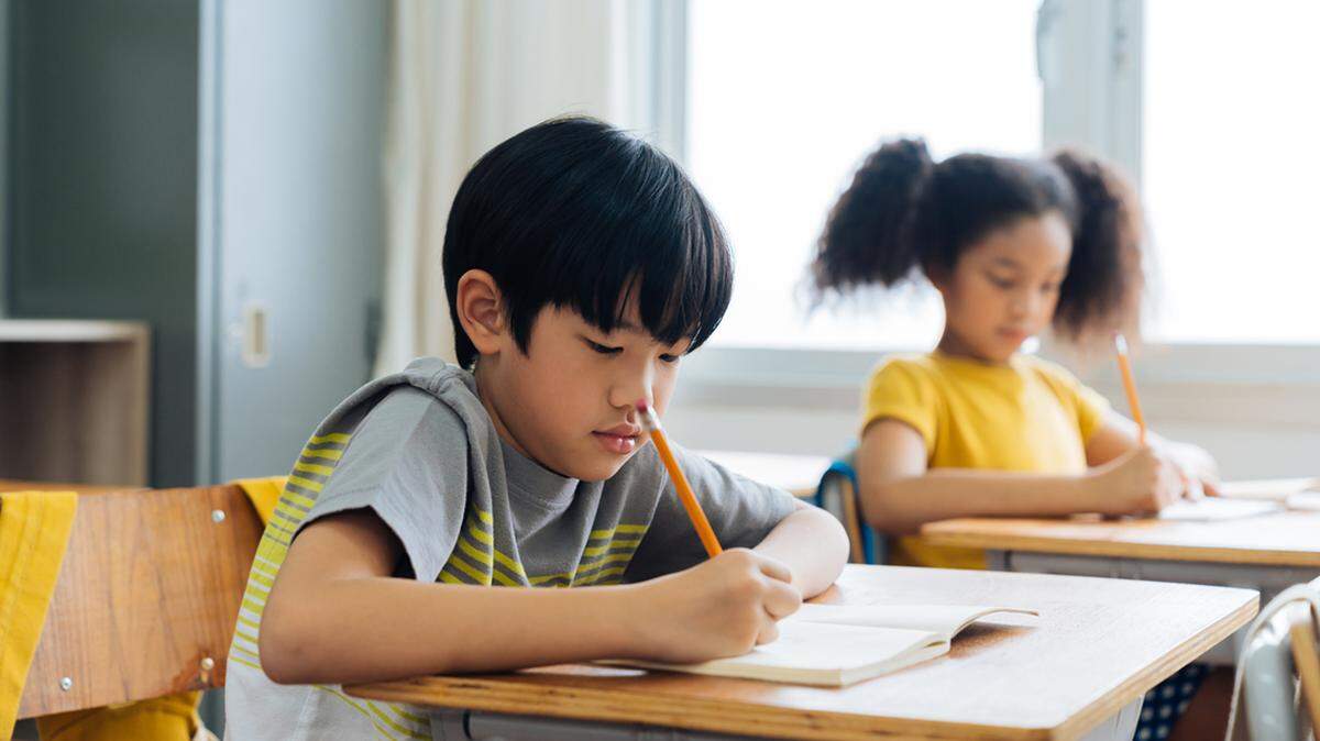 School children sitting at desk in school writing in note book with pencil, studying, education, learning. Male and female students in classroom. Boy and girl in elementary age test score