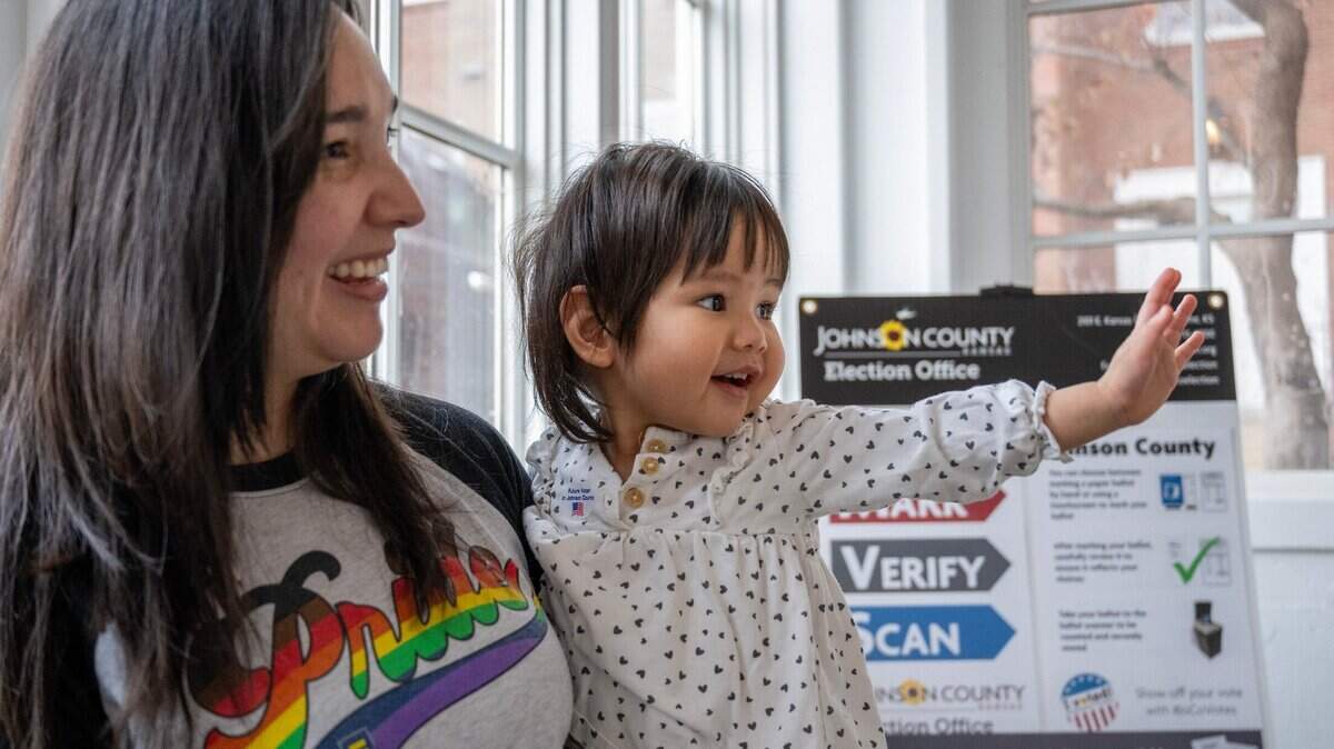 One-year-old Harley Nguyen waves to voters as her mother, Emily Nguyen, casts her ballot at Asbury United Methodist Church in Prairie Village on Tuesday.