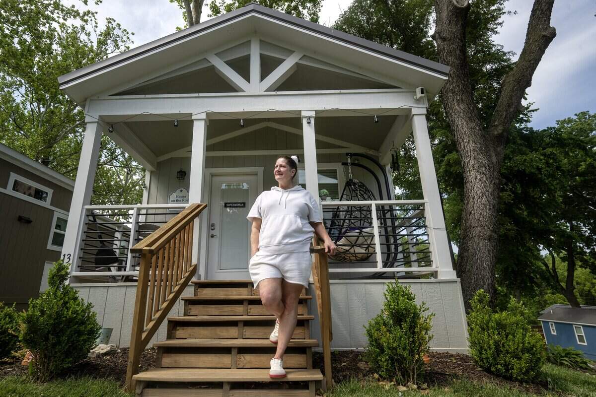 Cariann Lile, 56, looks out from outside her tiny home at Eden Village on Tuesday, May 12, 2026, in Kansas City, Kansas.  Lile, who experienced homelessness for six years before moving into the community in September 2024, says the stability feels like "winning the lottery."  Eden Village, 1001 Metropolitan Ave., has 22 tiny homes.