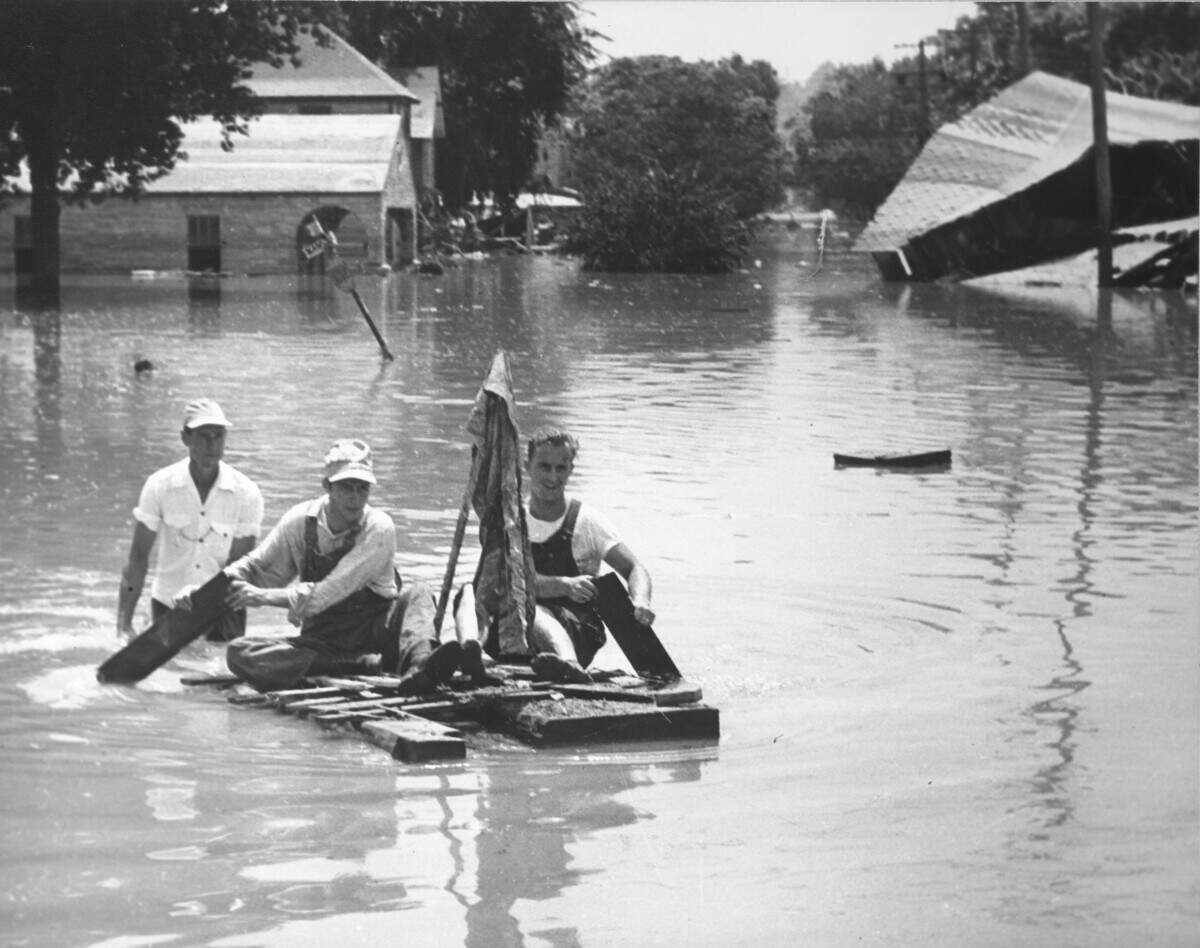 Men paddling a makeshift raft near Mill Street Bridge in Armourdale, Kan.