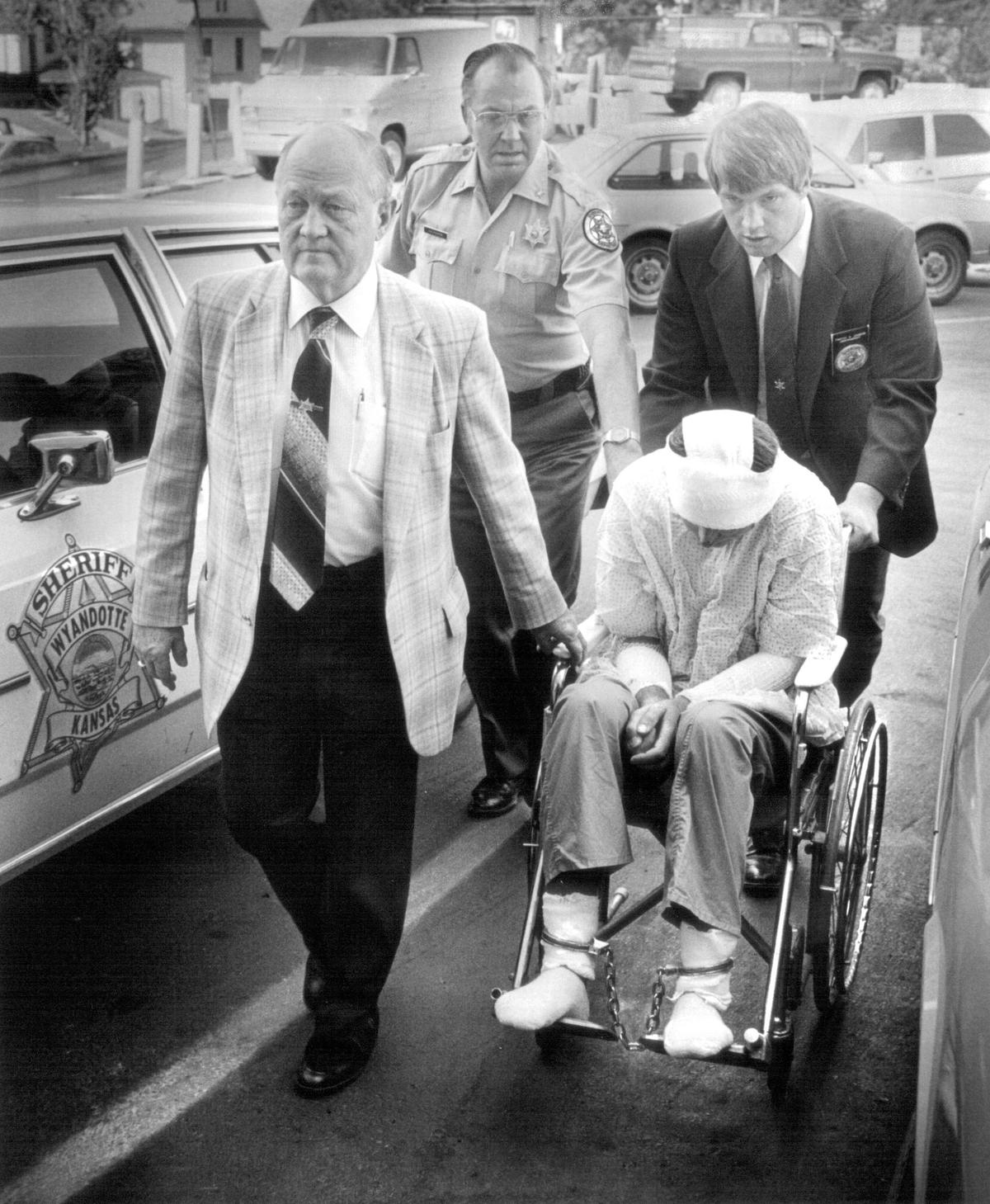Robert J. Gross was wheeled into the Wyandotte County Courthouse in 1984 by (from left) Wyandotte County Sheriff John Quinn, Deputy Arvol Pearon and Undersheriff Tim Johnson. Gross was charged with making a terroristic threat against a Wyandotte County woman. Earlier in the day he was released from the University of Kansas Medical Center, where he was undergoing burn treatment. Gross was later convicted of making the threats.