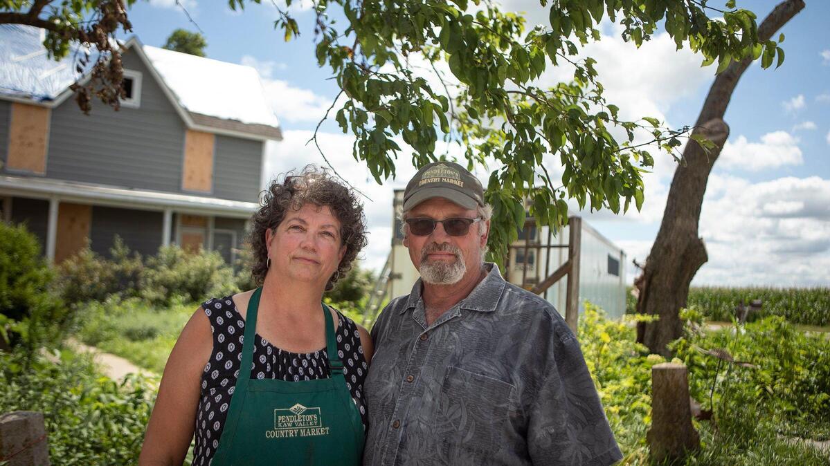 John and Karen Pendleton, owners of Pendleton’s Country Market, posed Monday in front of their house, which was hit by a tornado in May. Moving into a new home, cleaning up their farm and selling the crops they can save has left them no time to plant over the last six weeks.