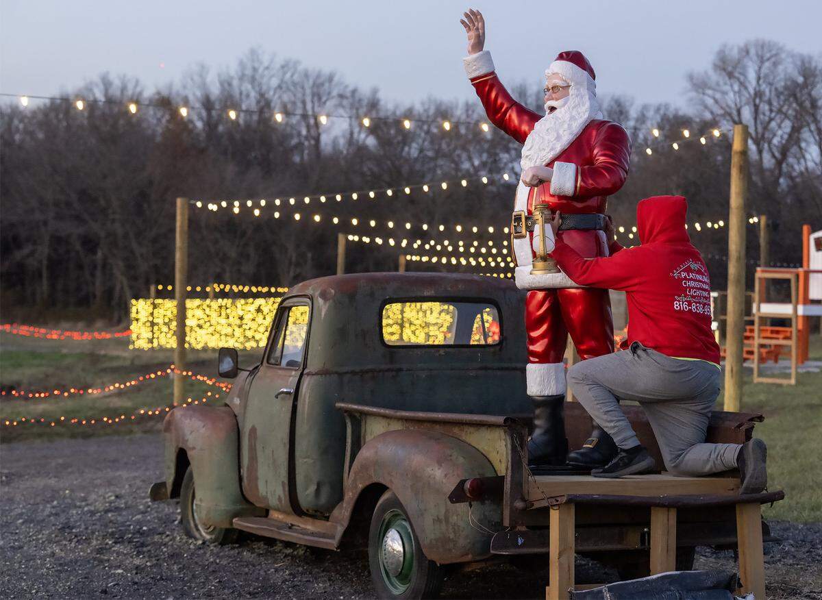 Jordan Adams of North Pole Acres sets up a Santa Claus in the bed of a 1951 pickup truck at dusk on Wednesday, Dec. 10, 2025, in Oak Grove, Missouri. North Pole Acres, 1010 NW 1st St., is an animated drive-through holiday display and is open to visitors Sunday through Friday, with an entry fee of $20 per car and $40 per commercial vehicle.