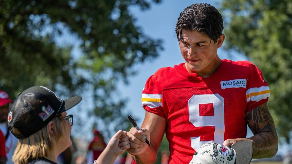 Kansas City Chiefs running back Louis Rees-Zammit gives a fist pump to a young fan while signing autographs after a practice at training camp. Rees-Zammit was a professional rugby player in England 
before working to get a spot with the Chiefs in American football.