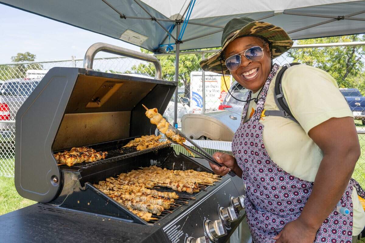 Sylvia Brown flips chicken skewers that will be served at the Puerto Rico vendor booth at the Ethnic Enrichment Festival in Swope Park on Saturday, Aug. 16, 2025, in Kansas City. The annual festival celebrates the many different cultures and ethnicities that exist in Kansas City, with vendor booths, cultural education opportunities, and performances. Temperatures reached nearly 100 degrees.