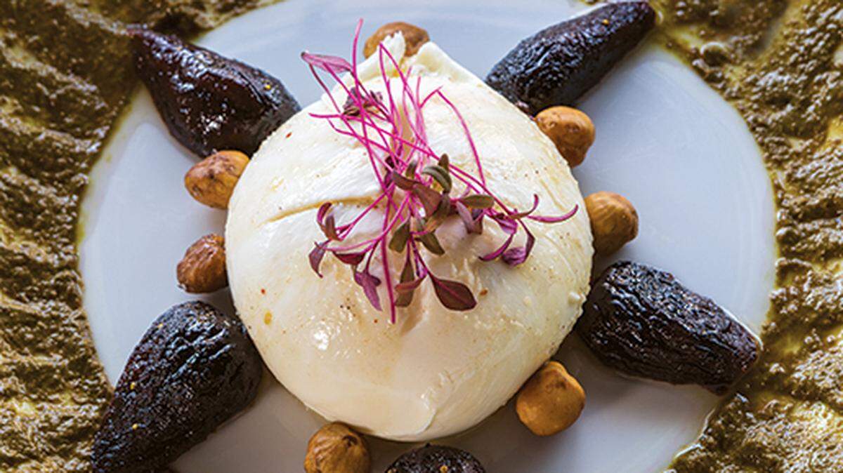 Plate serves Burrata cheese on beet green pesto with crostini, seared hazelnuts and grappa figs.