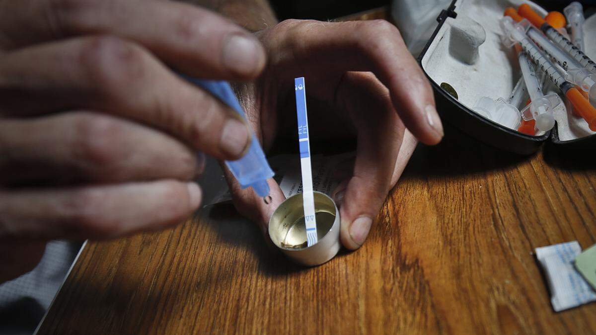 An addict prepares heroin, placing a fentanyl test strip into a mixing container to check for contamination, Wednesday Aug. 22, 2018, in New York. If the strip registers a “pinkish” to red marker then the heroin is positive for contaminants. 