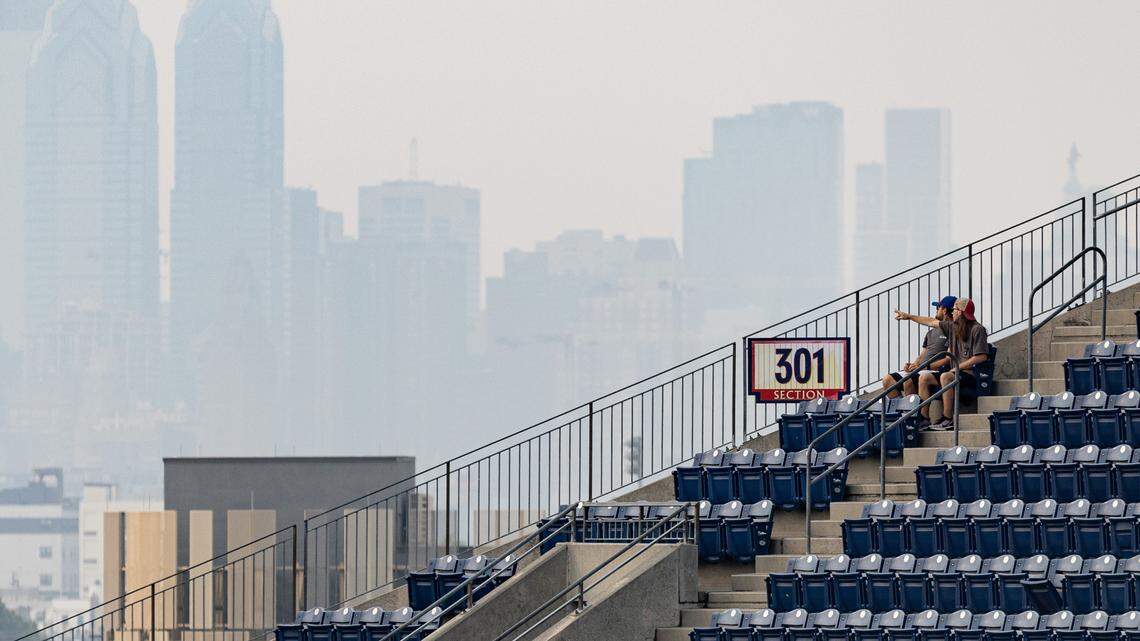 Two fans look out in the direction of center city Philadelphia as it is obscured by the smoke from Canadian wildfires before a game between the Philadelphia Phillies and the Detroit Tigers at Citizens Bank Park on June 8, 2023.